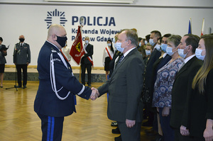 Komendant Wojewódzki policji w Gdańsku składa gratulacje jednemu z pracowników cywilnych. Panowie podają sobie dłoń.