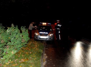 Noc. Policyjny radiowóz zaparkowany na poboczu drogi poza obszarem zabudowanym. Policjant rozmawia z mężczyzną, który nie posiadał elementów odblaskowych.