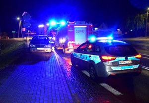 Radiowóz policyjne oraz wóz straży pożarnej na miejscu zdarzenia. Auta mają włączone światła błyskowe.