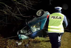 Policjant w odblaskowej kamizelce patrzy na leżącego na dachu forda.