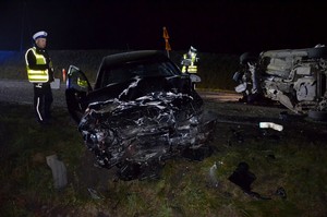 Policjanci z drogówki pracują na miejscu wypadku. W tle rozbite auta osobowe.