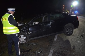 Policjanci z drogówki pracują na miejscu wypadku. W tle rozbite auta osobowe.