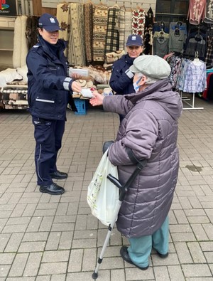 Policjantki wręczają seniorce maseczkę do zasłaniania ust i nosa.