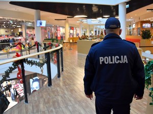 Policjant patroluje korytarz w galerii handlowej. Na zdjęciu widoczne są elementy świątecznego wystroju.