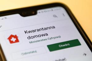 Grafika obrazkowa. Telefon komórkowy wyświetla ekran główny aplikacji Kwarantanna Domowa.