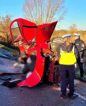 Policjanci prowadzą oględziny rozbitej toyoty. Auto posiada znaczne uszkodzenia karoserii. Część z nich powstała podczas cięcia auta przez ratowników.