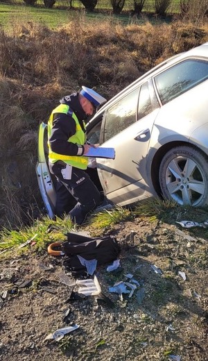Policjant prowadzi oględziny skody. Auto znajduje się w przydrożnym rowie.