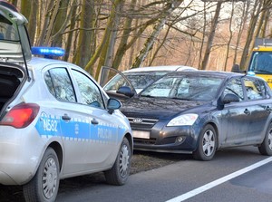 Zdjęcie wykonane w miejscu interwencji. Oznakowany radiowóz z włączonymi światłami błyskowymi, a za nim odzyskana przez funkcjonariuszy mazda.