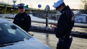 Policjanci z drogówki stoją przy zaparkowanym pojeździe służbowym.