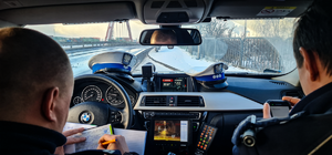 Zdjęcie wykonane z wewnątrz radiowozu. Policjanci sporządzają dokumentację z kontroli drogowej.