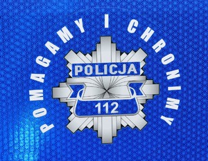 Odblaskowy logo na drzwiach radiowozu policyjnego z napisem o treści: Pomagamy i Chronimy.