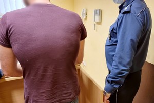 Mężczyzna doprowadzony do policyjnego aresztu, gdzie policjanci sporządzają z dokumentację.
