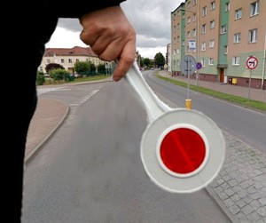 Policjant z lizakiem, po prawej stronie ulicy znak zakazujący skrętu w lewo.