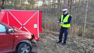 Zdjęcie rozbitego chevroleta. W pobliżu policjant drogówki prowadzi czynności służbowe.