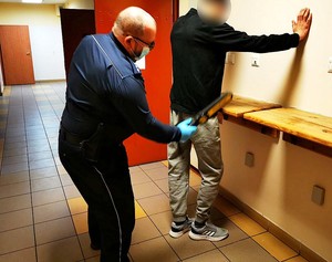Policjant przeszukuje zatrzymanego mężczyznę.
