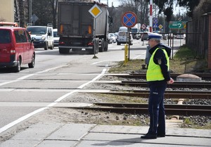 Policjant przygląda się pojazdom przejeżdżającym przez przejazd kolejowy.
