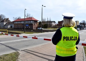 Policjantka w żółtej kamizelce odblaskowej stoi przy szlabanie kolejowym.