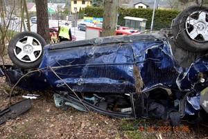 Leżące na dachu audi, wśród drzew. Widok uszkodzonego boku pojazdu.