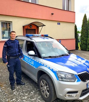 Policjant stoi przy radiowozie oznakowanym.