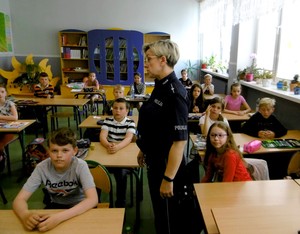 Sala lekcyjna. Dzieci w ławkach. Policjantka prowadzi zajęcia z uczniami.