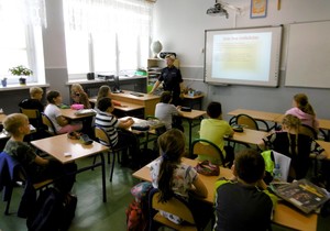 Sala lekcyjna. Dzieci w ławkach. Policjantka prowadzi zajęcia z uczniami.