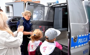 Policjantka pokazuje dzieciom klatkę radiowozu, która sluży do przewożenia osób zatrzymanych.