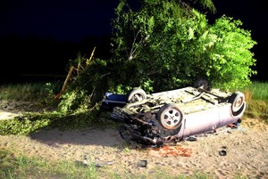 Noc. Drzewo oraz leżący w pobliżu niego na dachu rozbity opel.