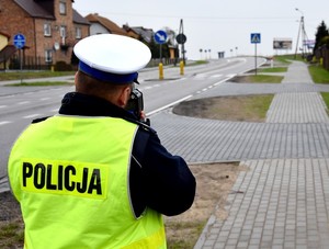 Policjant pełni służbę w rejonie przejścia dla pieszych oczekując z radarem na kierujących, którzy nie stosują się do obowiązujących prędkości.