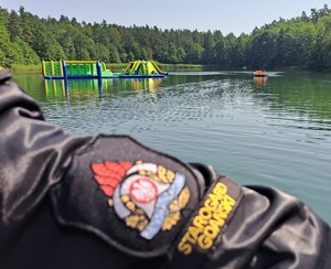 Naszywka na rękawie munduru strażaka z oznaczeniem starogardzkiej jednostki, na tle jeziora, trzcin i lasu.