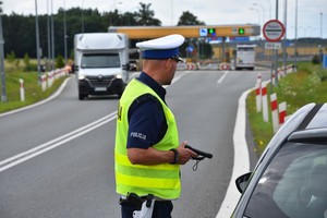 Policjant w trakcie kontroli drogowej. W tle widoczne bramki wjazdowe na autostradę A1.
