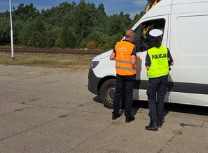 Policjantka z przedstawicielem PKP rozmawiają z kierowcą dużego białego busa.