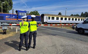 Policyjny radiowóz i stojące w pobliżu policjantki, które spoglądają na przejeżdżający pociąg.