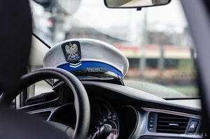 Czapka służbowa policjanta z drogówki leży na desce rozdzielczej policyjnego radiowozu.