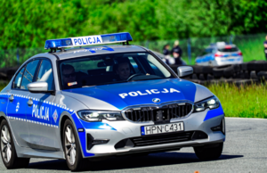 Policjantka kieruje radiowozem policyjnym. Tło zdjęcia jest rozmazane.