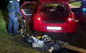 Policjant z psem w trakcie przeszukania samochodu. W tle panujące ciemności.