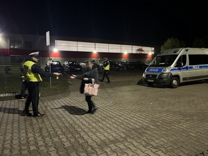 Policjanci wręczają przybywającym do pracy pracownikom elementy odblaskowe.