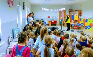 Dzielnicowa w przedszkolu rozmawia z dziećmi. Po prawej stronie przekazane znaki drogowe.