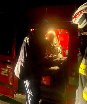 Policjant i strażak stoją przy samochodzie straży pożarnej, w którym siedzi odnaleziony mężczyzna.