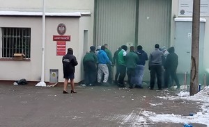 Grupa osób w kominiarkach, rzucająca świece dymne, próbująca sforsować główną bramę aresztu.