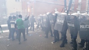 Po lewej stronie zdjęcia grupa agresywnych osób naciera na idących w kordonie policjantów.