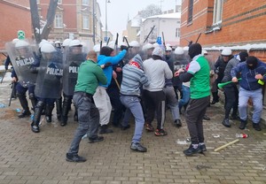 Grupa agresywnych mężczyzn w kominiarkach, próbuje przedostać się siłowo przez policyjny kordon.