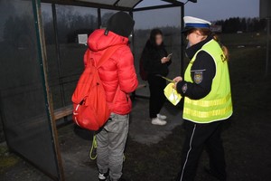 Policjantka wręcza odblaski osobie oczekującej na przystanku autobusowym.