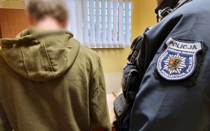 Stojący po prawej stronie policjant nadzoruje osadzanie zatrzymanego do policyjnego aresztu. Zdjęcie wykonane w pomierzeniu dla osób zatrzymanych.