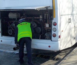 Policjant w żółtej kamizelce odblaskowej z napisem policja kontroluje autokar wycieczkowy.