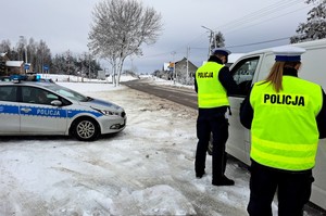 Policjanci w żółtych odblaskowych kamizelkach rozmawiają z kierowcą kontrolowanego pojazdu. Dookoła zimowa aura.