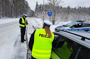 Policjanci w żółtych odblaskowych kamizelkach rozmawiają z kierowcą kontrolowanego pojazdu. Dookoła zimowa aura.