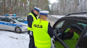 Policjanci w żółtych odblaskowych kamizelkach rozmawiają z kierowcą kontrolowanego pojazdu. Dookoła zimowa aura.