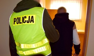 Policjant wprowadza podejrzanego do pomieszczenia dla osób zatrzymanych.