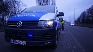 Policyjny radiowóz z niskiej perspektywy, a za nim policjant drogówki w żółtej kamizelce odblaskowej.