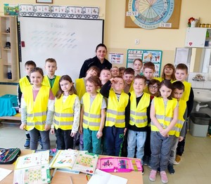 Zdjęcie grupowe z policjantką. Dzieci w żółtych kamizelkach odblaskowych.